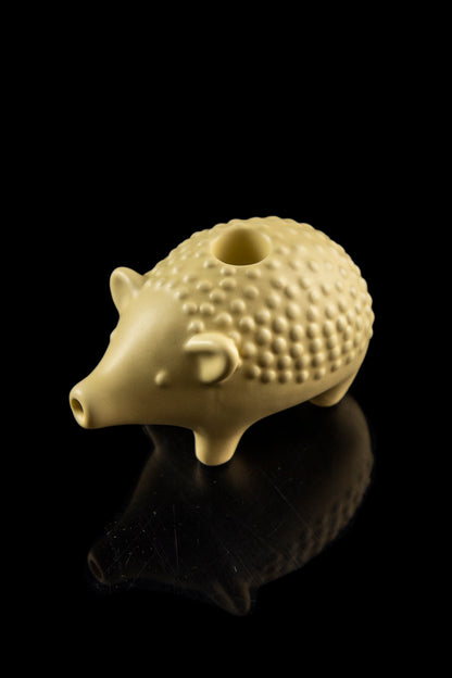 Ceramic pig-shaped smoking pipe with a glossy finish, reflected on a black surface.