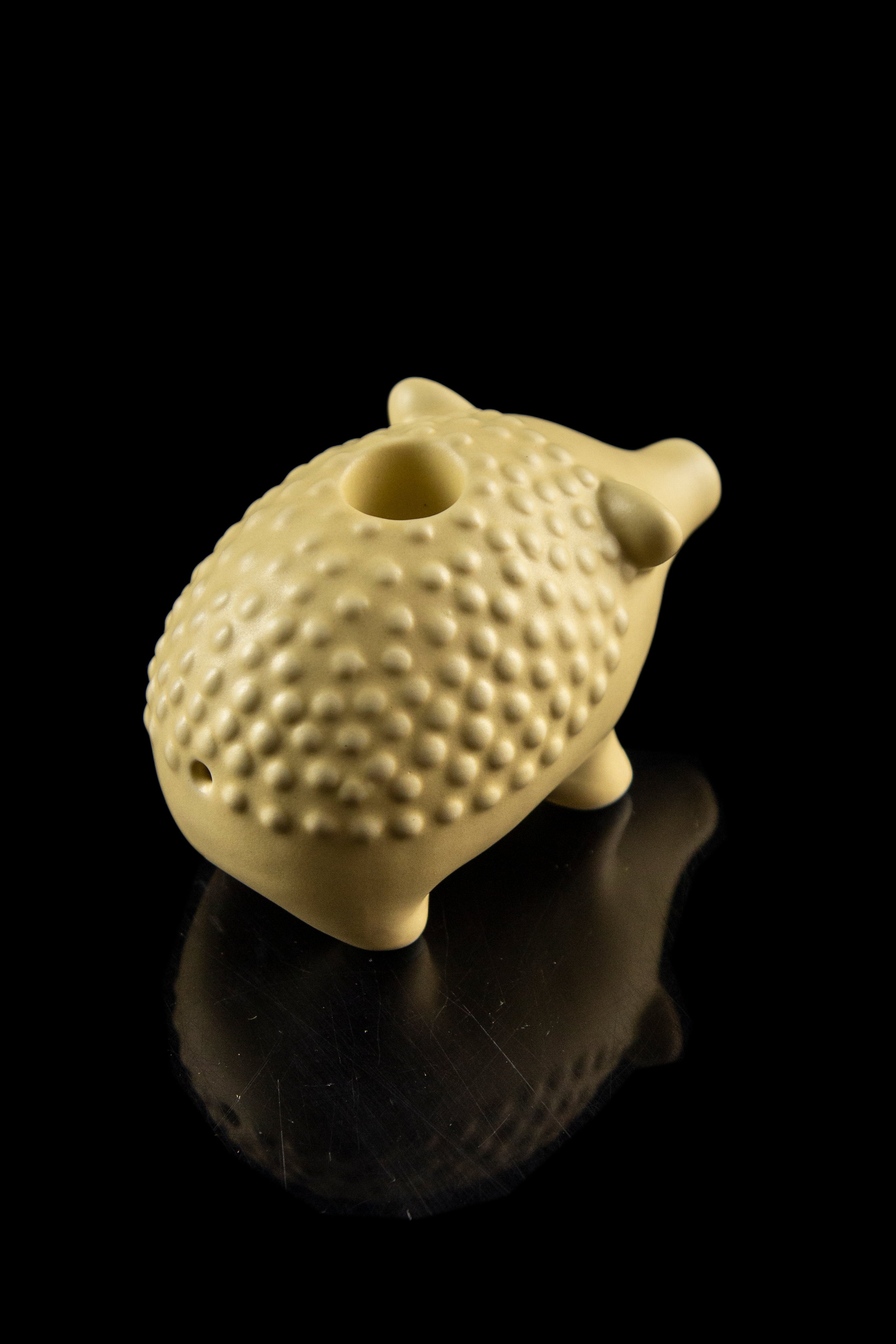 Ceramic cannabis pipe shaped like a pig with a textured surface, displayed on a reflective black surface.