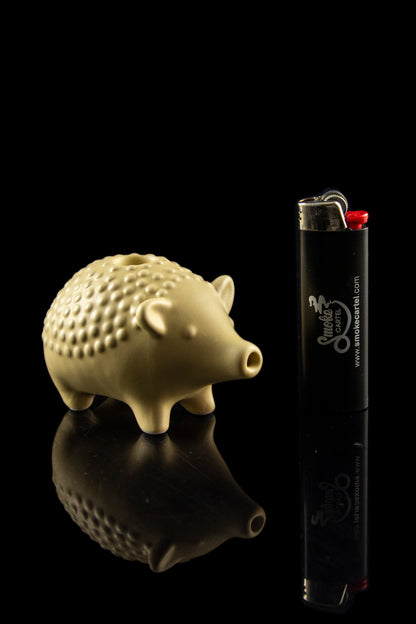Ceramic pig-shaped pipe and lighter reflected on a black surface.