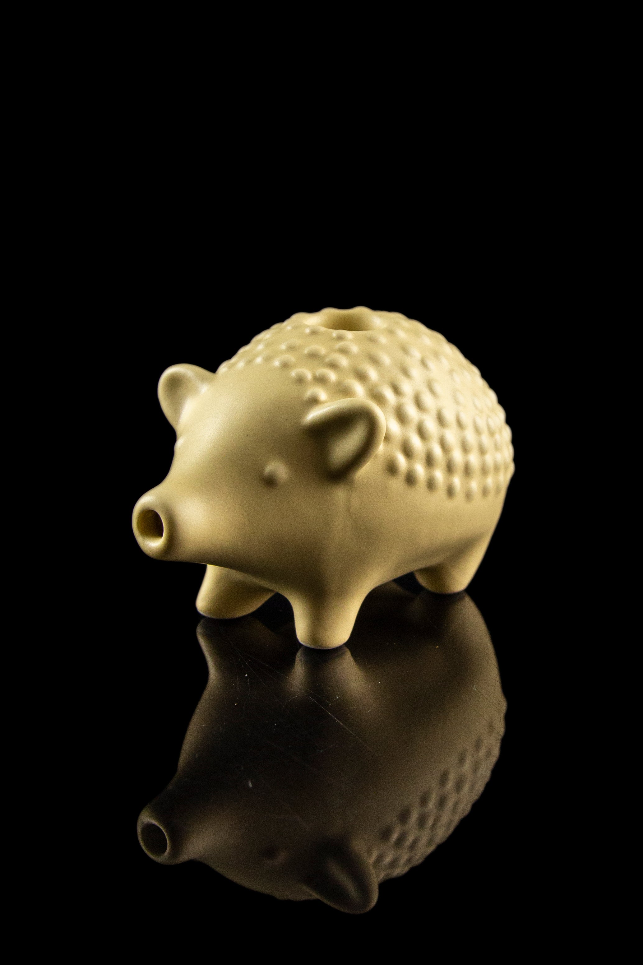 Gold ceramic pig-shaped pipe with a glossy reflection on a black surface.