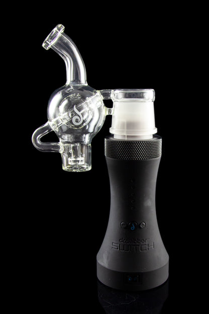 Clear glass bubbler attachment connected to a black electronic dab rig, reflecting on a glossy surface.