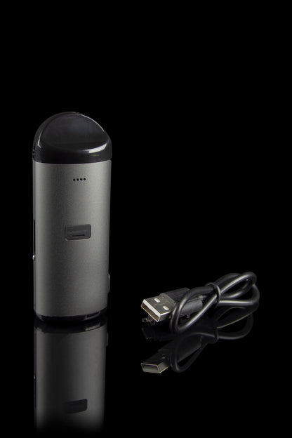 Sleek, metallic cannabis vaporizer pen with a USB charging cable, displayed on a reflective black surface.