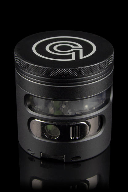 Black metal cannabis grinder with a clear viewing window, showcasing ground plant material inside."