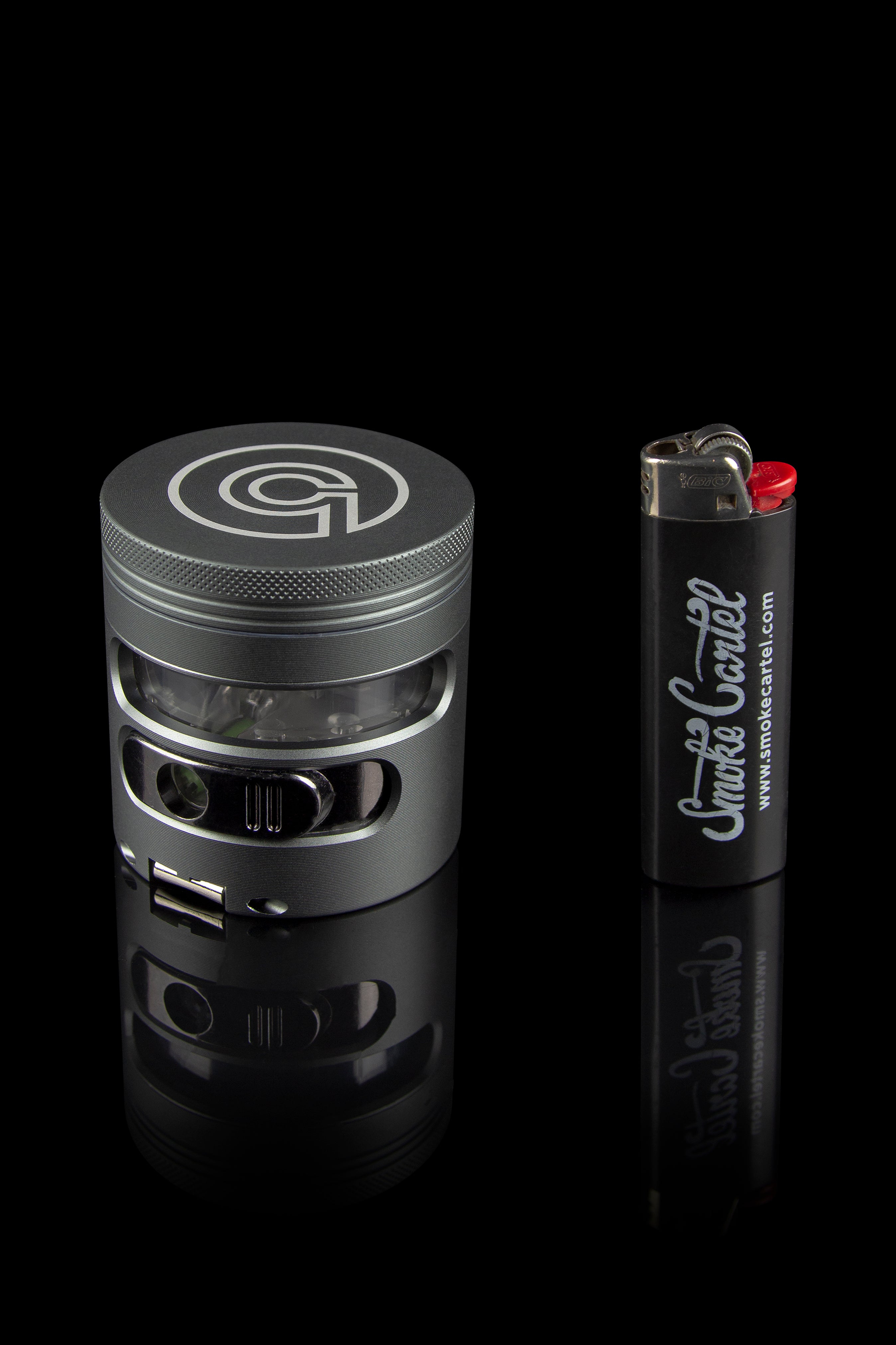 Black metal grinder and lighter with "Smoke Cartel" branding on a reflective surface.