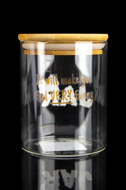 Clear glass jar with a bamboo lid and the text “It will make you feel VERY Funny” displayed on the front, reflected on a black surface.