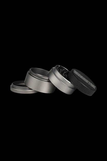 A top-down view of the four pieces of the Kannastor 4-Piece Solid Body Grinder, disassembled on a dark surface.