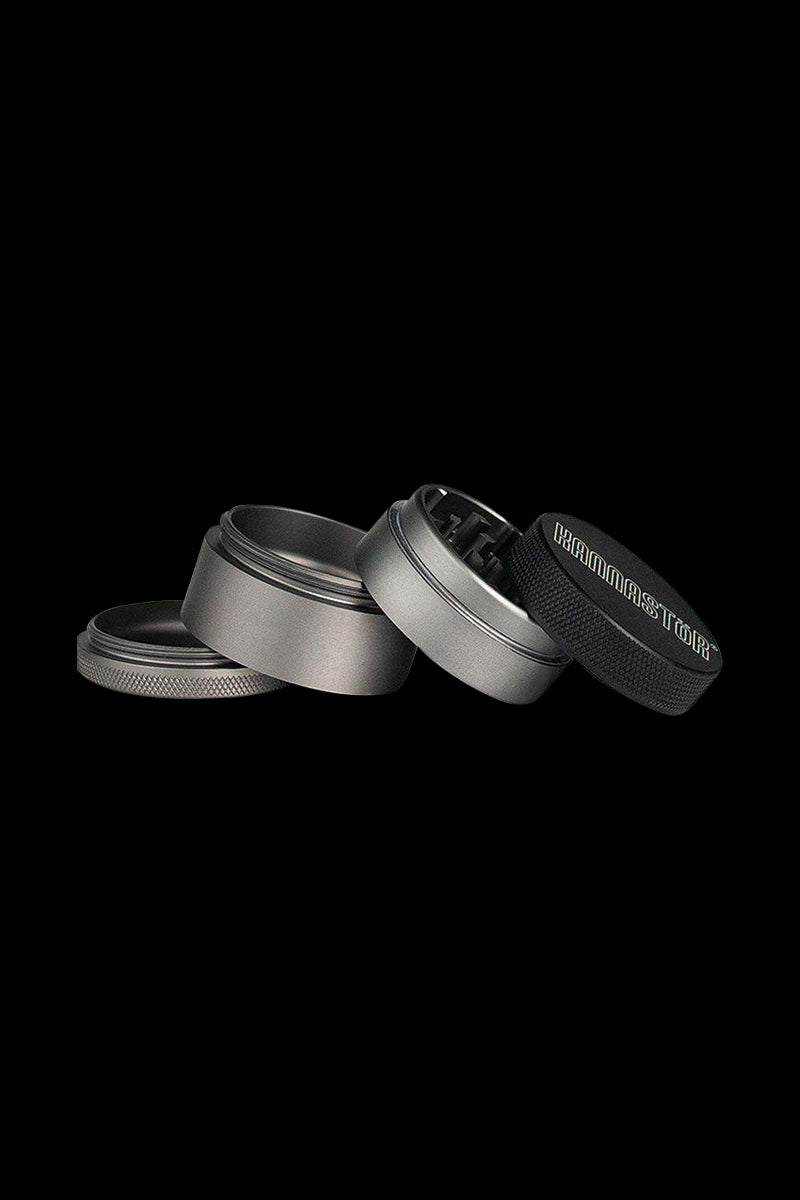 A top-down view of the four pieces of the Kannastor 4-Piece Solid Body Grinder, disassembled on a dark surface.