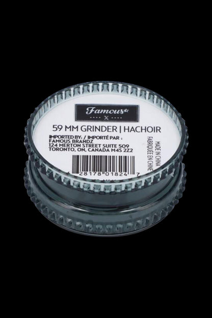 Close-up of a metallic cannabis grinder with label details including "59 MM GRINDER" and import information.