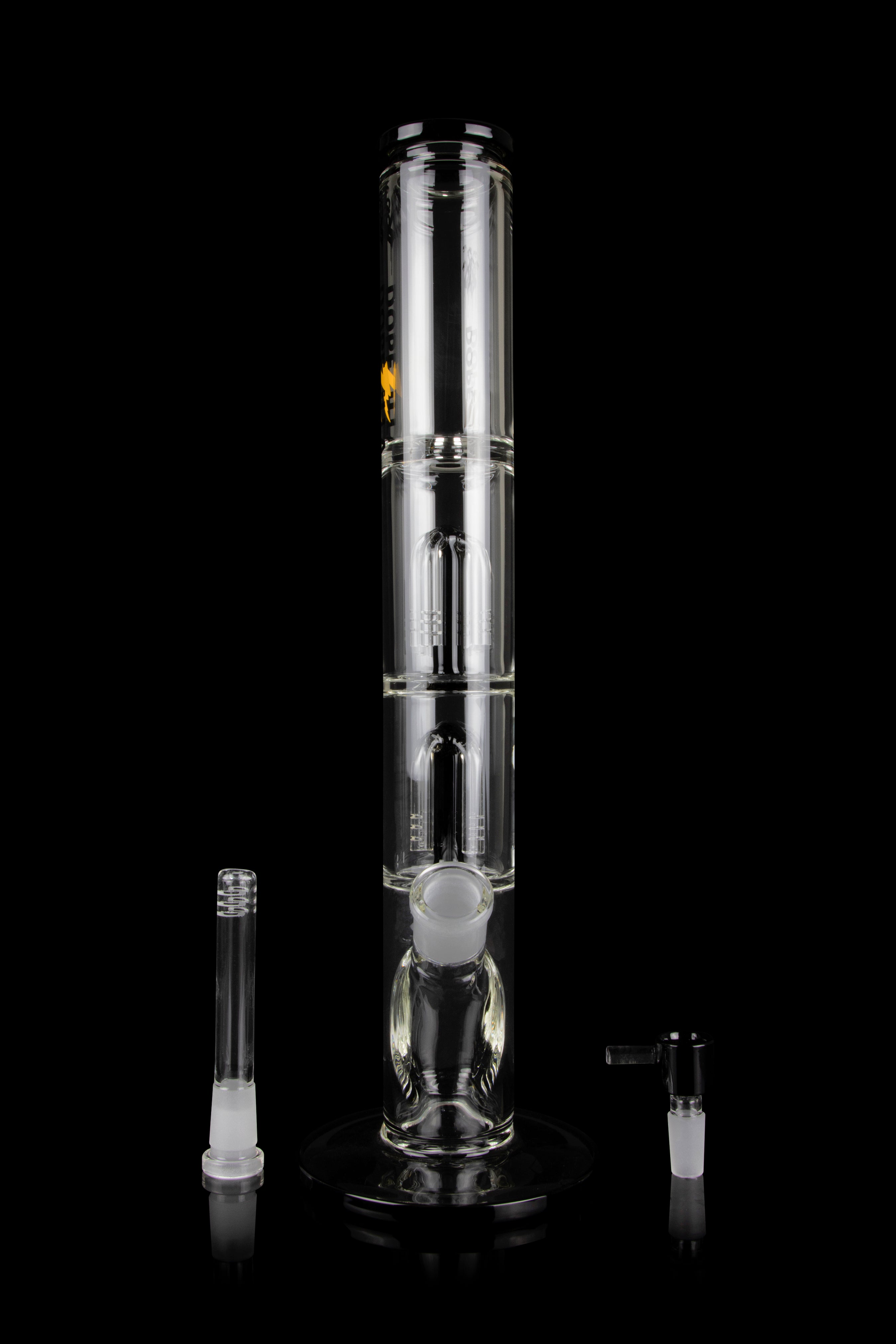 Clear glass bong with multiple filtration chambers and accompanying glass pieces, displayed on a reflective surface against a black background.