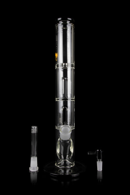 Clear glass bong with multiple filtration chambers and accompanying glass pieces, displayed on a reflective surface against a black background.