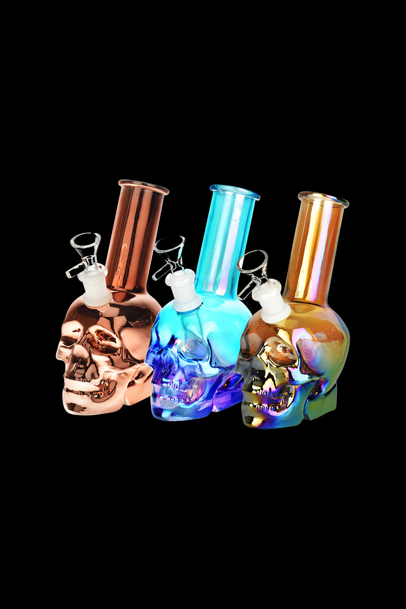 Front view of the Metallic Sunset Skull Water Pipe, showcasing a sculpted glass skull with a gradient finish against a dark background.