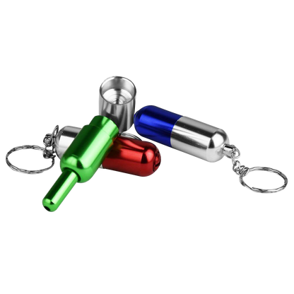 Angled close-up of three brightly anodized Pill Transformer Metal Hand Pipe keychain capsules in green, red and blue on a white background