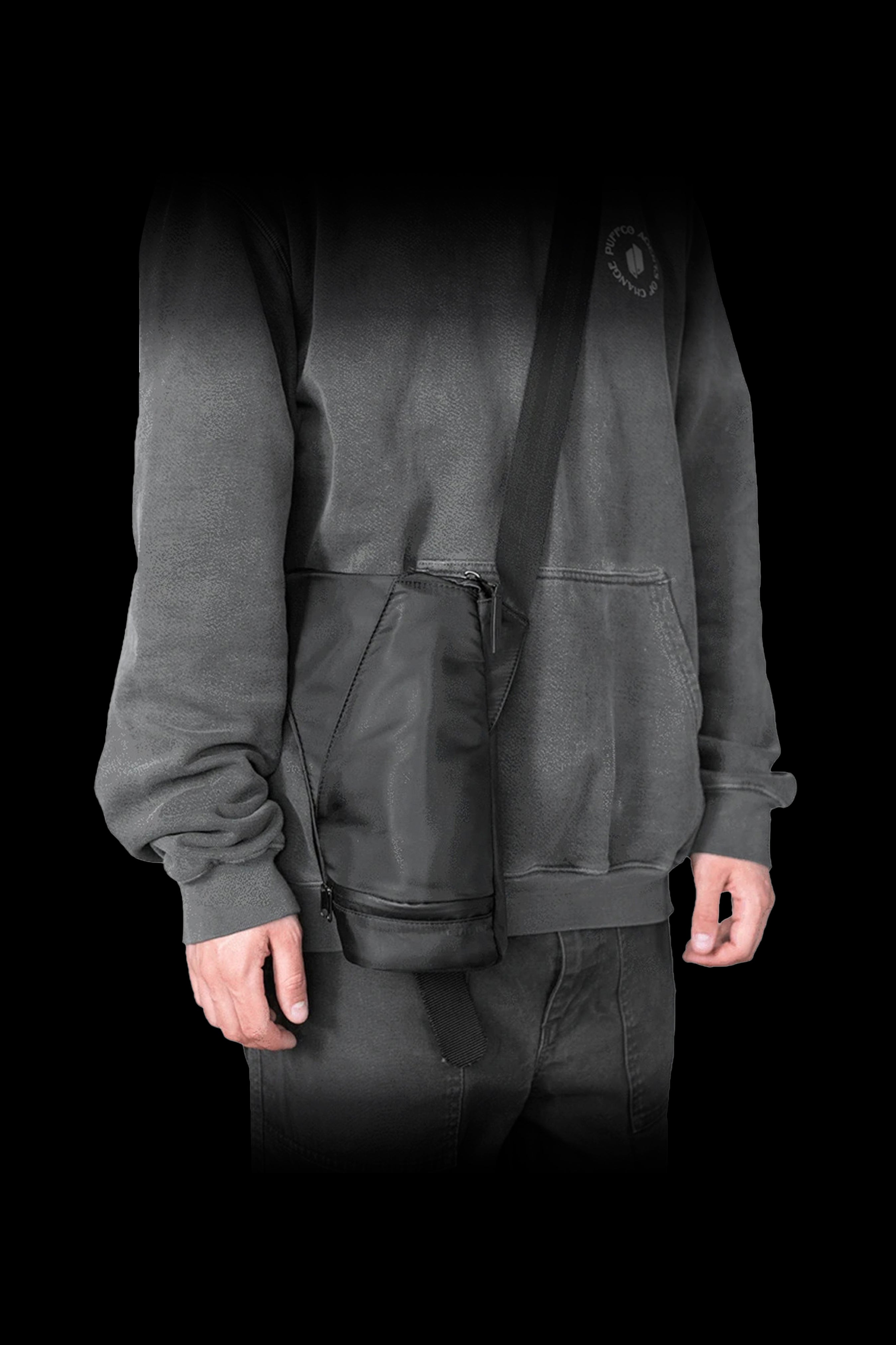 A person wearing a dark gray hooded sweatshirt and pants, with a cannabis accessories carrying case slung across their body.