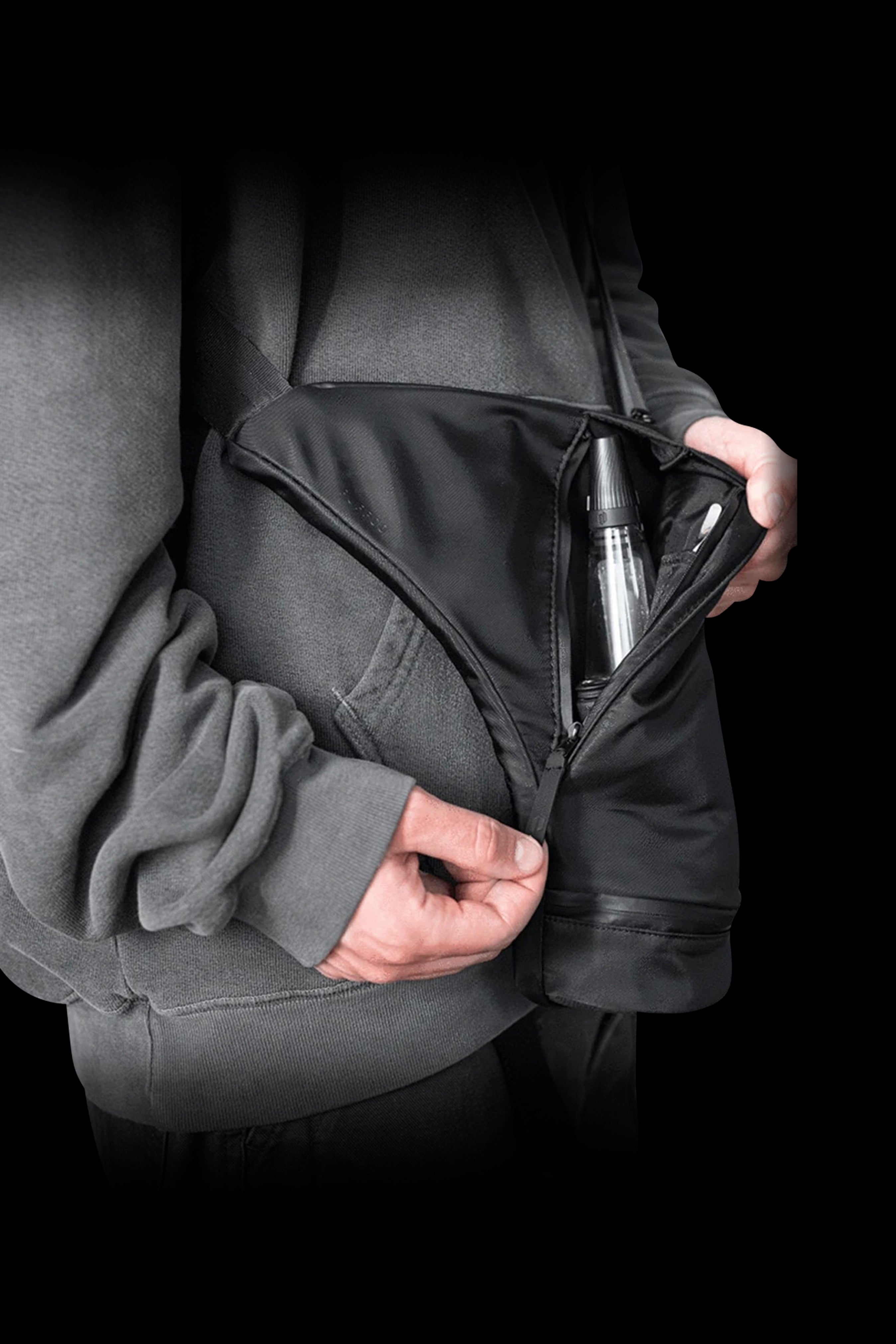 Close-up of a hand partially unzipping a pocket in a dark hooded sweatshirt, revealing a cannabis vape pen inside.