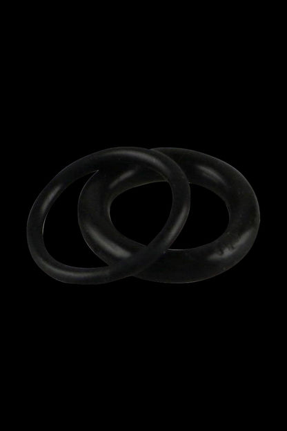 Close-up of two black Pulsar APX Wax/Barb Coil Replacement O-Rings - 2 Pack overlapped on a dark background, lit from above.