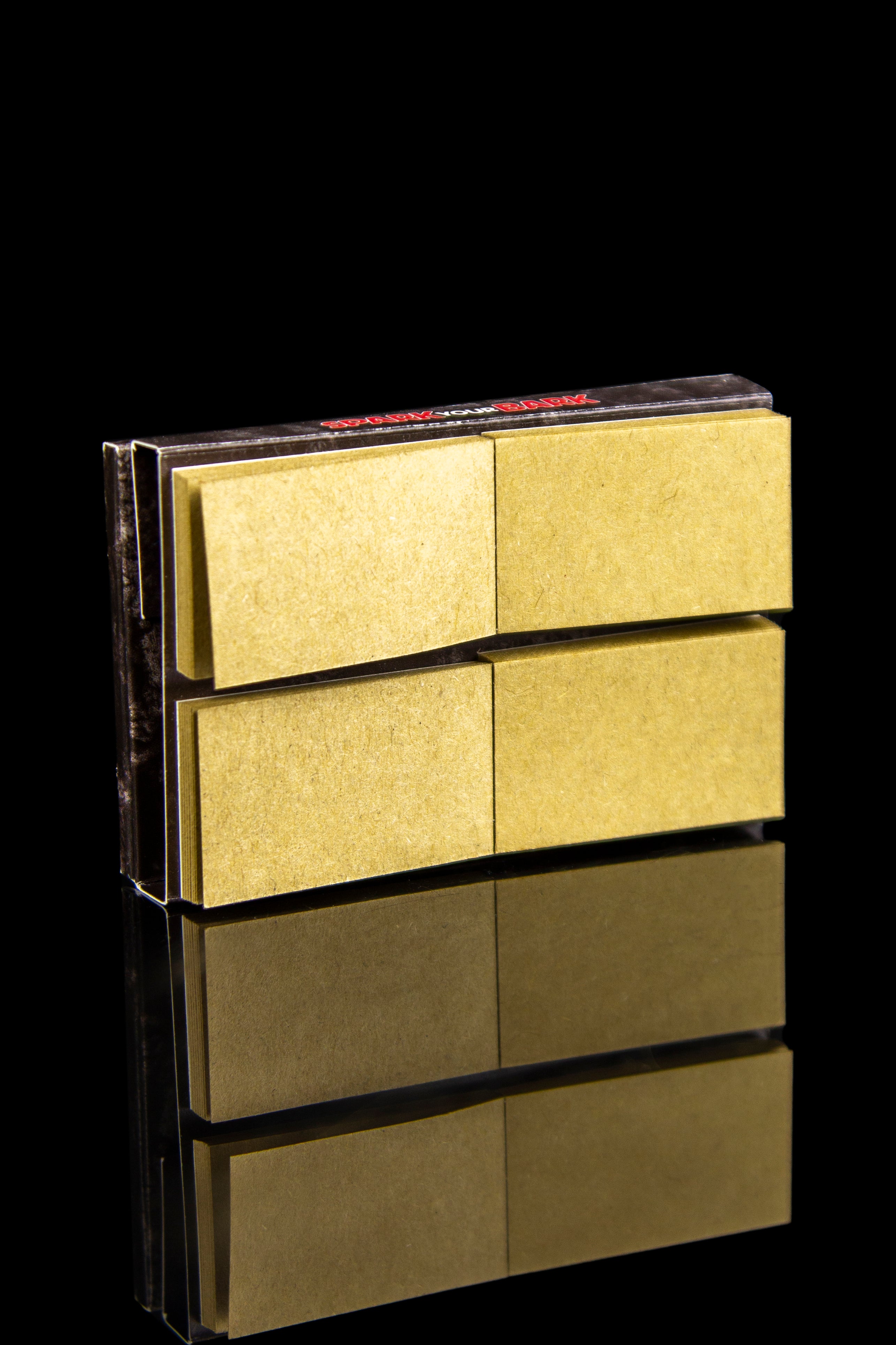 Gold rolling paper booklets stacked with a mirrored reflection on a black background.