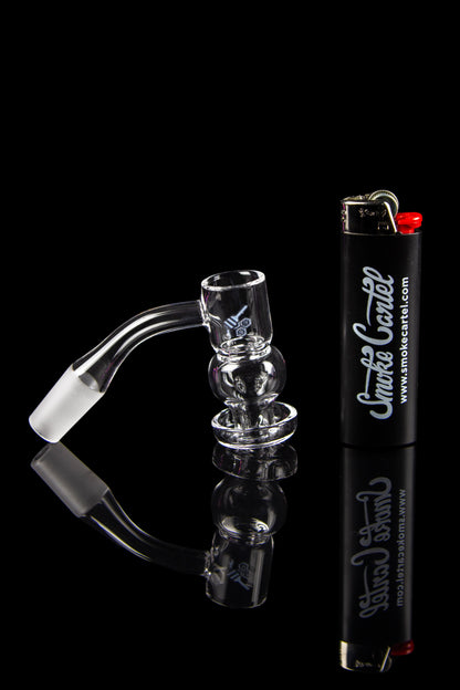 Clear glass dab rig with a quartz banger and lighter, reflected on a black surface with branding.