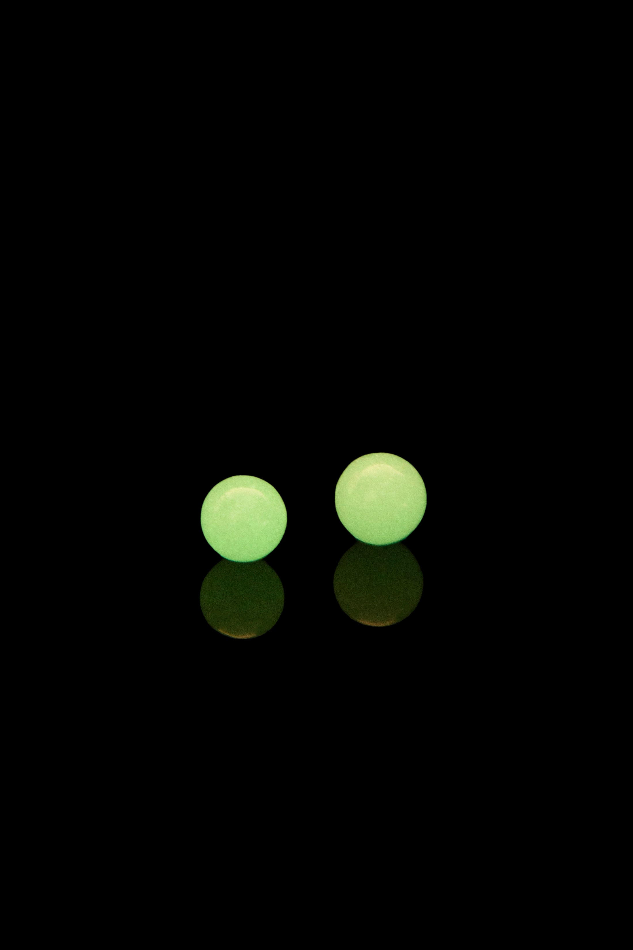 Two green cannabis rosin pills with reflections on a black background.