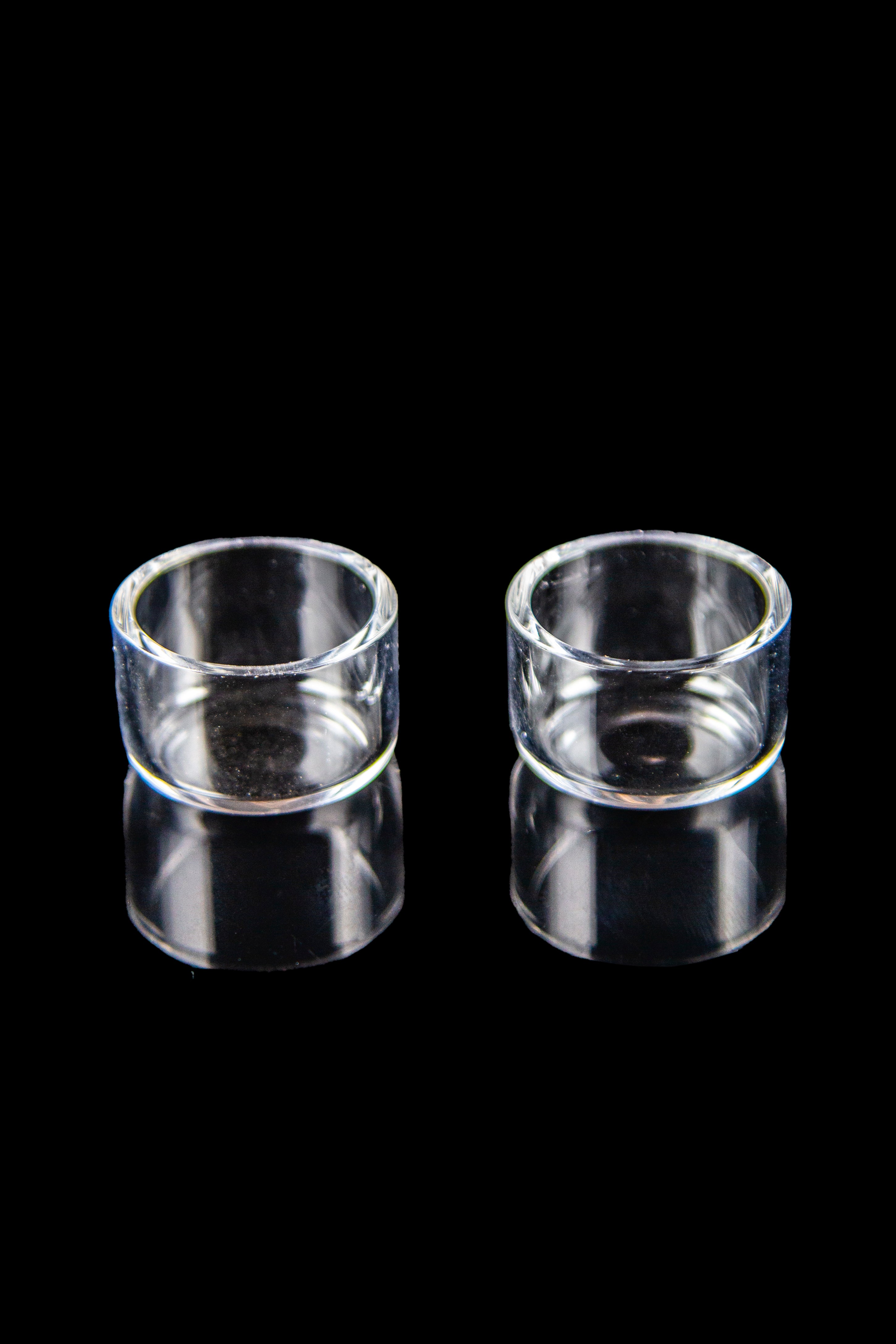 Two clear glass inserts for use with cannabis dab rigs, displayed on a black reflective surface.