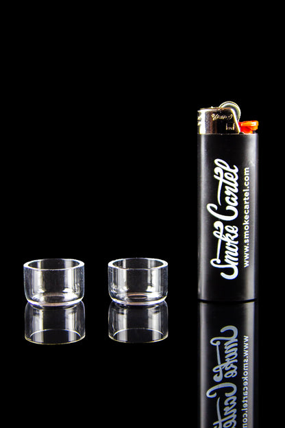 Two clear glass cannabis concentrate containers and a black lighter with “Smokecartel.com” printed in script, reflected on a glossy black surface.