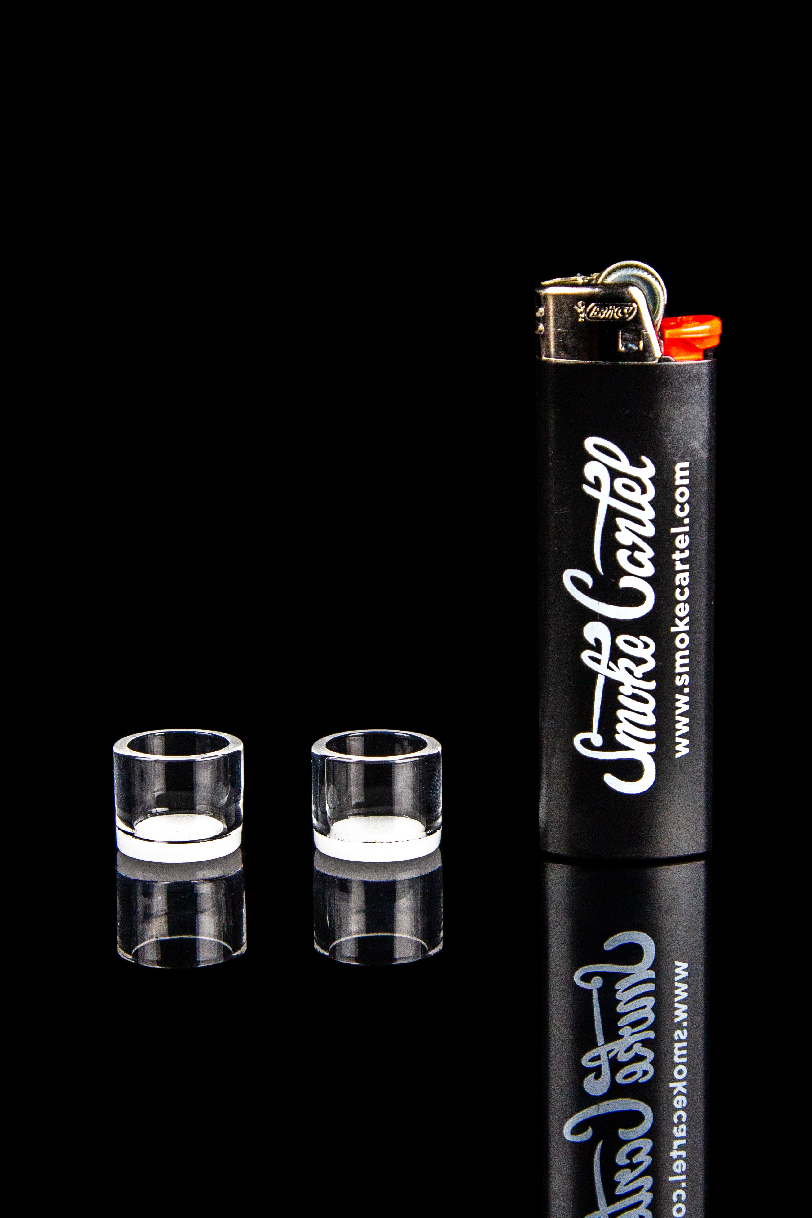 Two clear cannabis oil burners and a branded lighter against a black reflective surface.