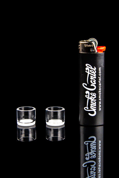 Two clear cannabis oil burners and a branded lighter against a black reflective surface.