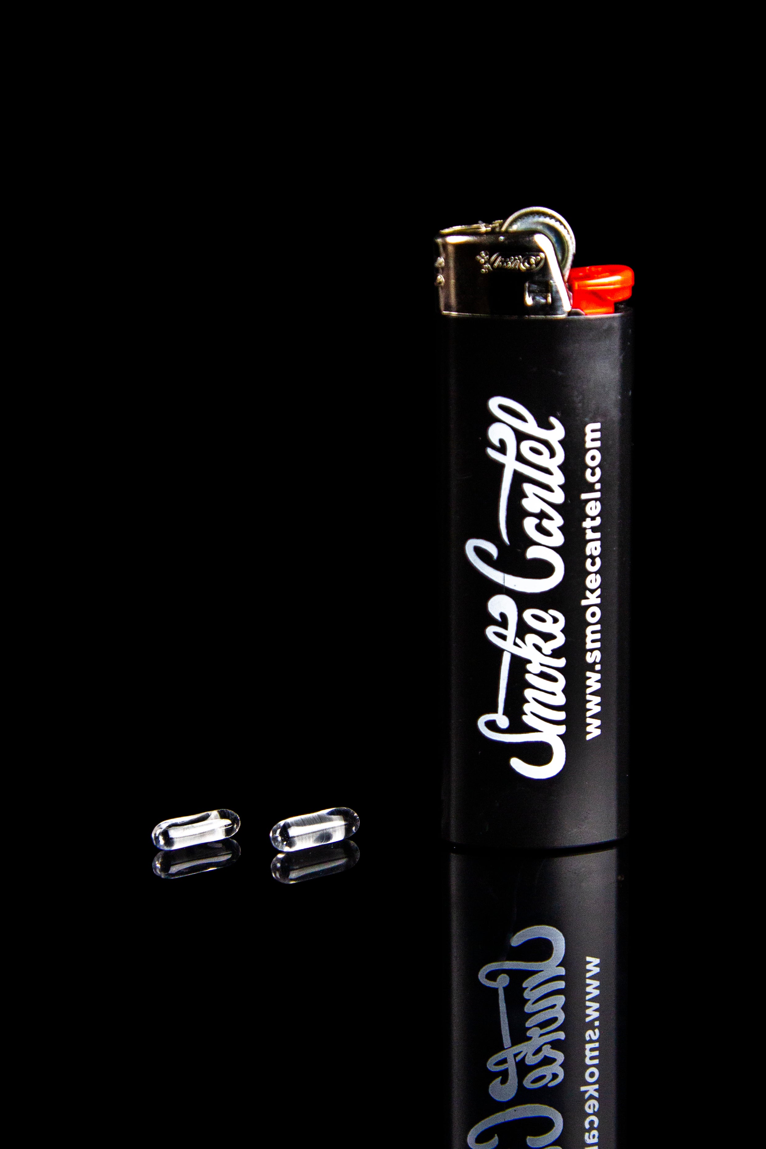 Black lighter with “Smoke Cartel” branding and two replacement butane refills against a dark background.