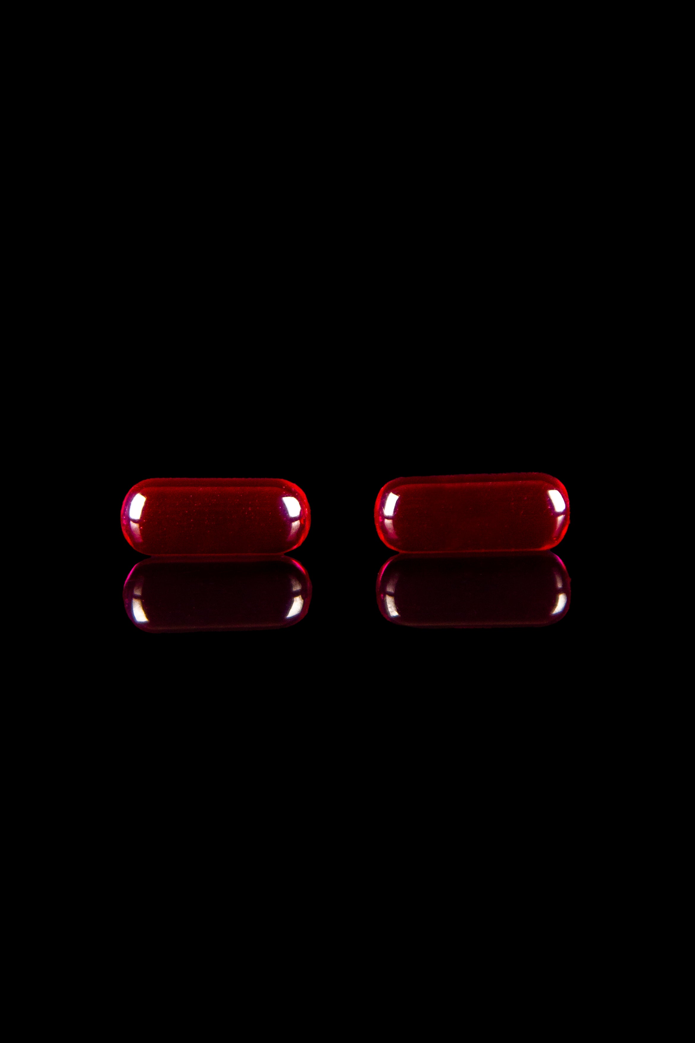 Two red cannabis capsules with reflections on a black background.