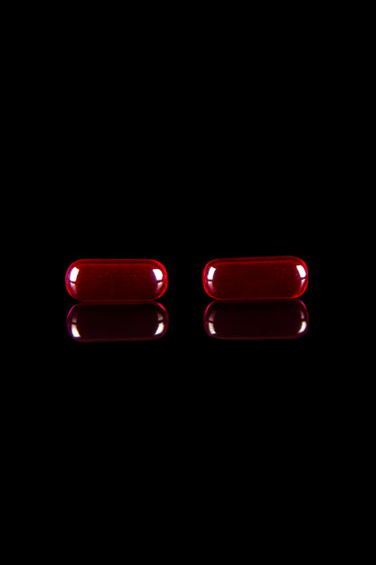 Two red cannabis capsules with reflections on a black background.