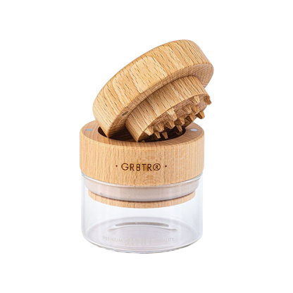 A close-up, top-down view of the RYOT Beech Wood GR8TR Grinder with Glass Jar, showing its textured wood lid and clear glass base.