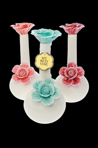 Three glass cannabis water pipes decorated with sculpted pink and teal roses against a black background, branded “My Bud Vase”.