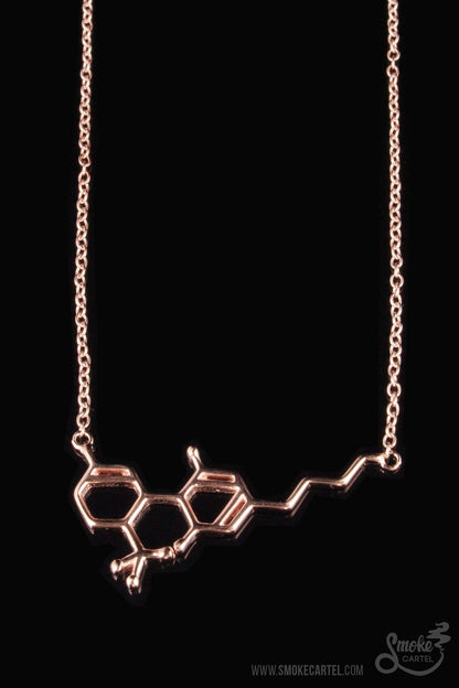 The Smoke Cartel THC Molecule Necklace, a delicate gold pendant, is displayed against a dark background.
