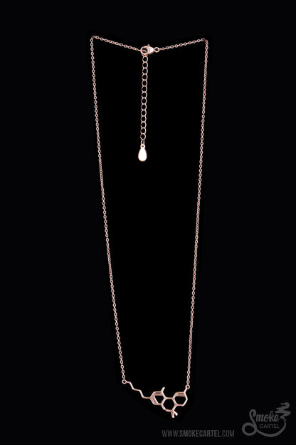 A close-up of the Smoke Cartel THC Molecule Necklace, a delicate silver pendant hanging from a fine chain against a dark background.