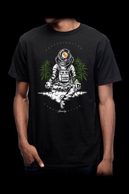 A man wearing a black t-shirt featuring a detailed illustration of an astronaut in a meditative pose surrounded by cannabis leaves.