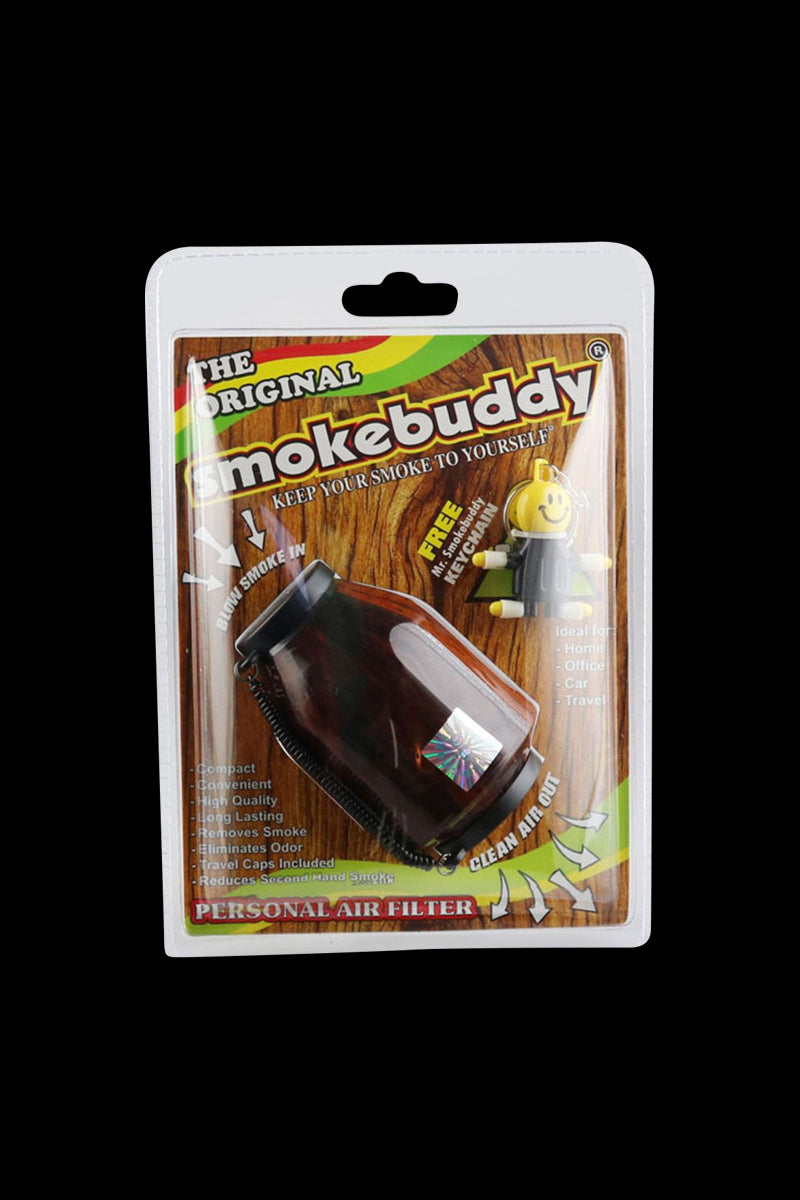 Front-facing shot of the Smokebuddy Original Personal Air Filter in clear clamshell packaging against a black background, showing the brown filter and colorful wood-grain backing.