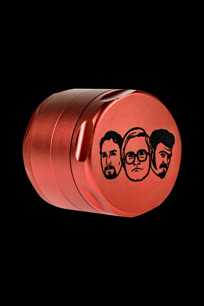 Red metal grinder with portraits of the cast from the film “Pineapple Express” etched on the lid, isolated on a black background.