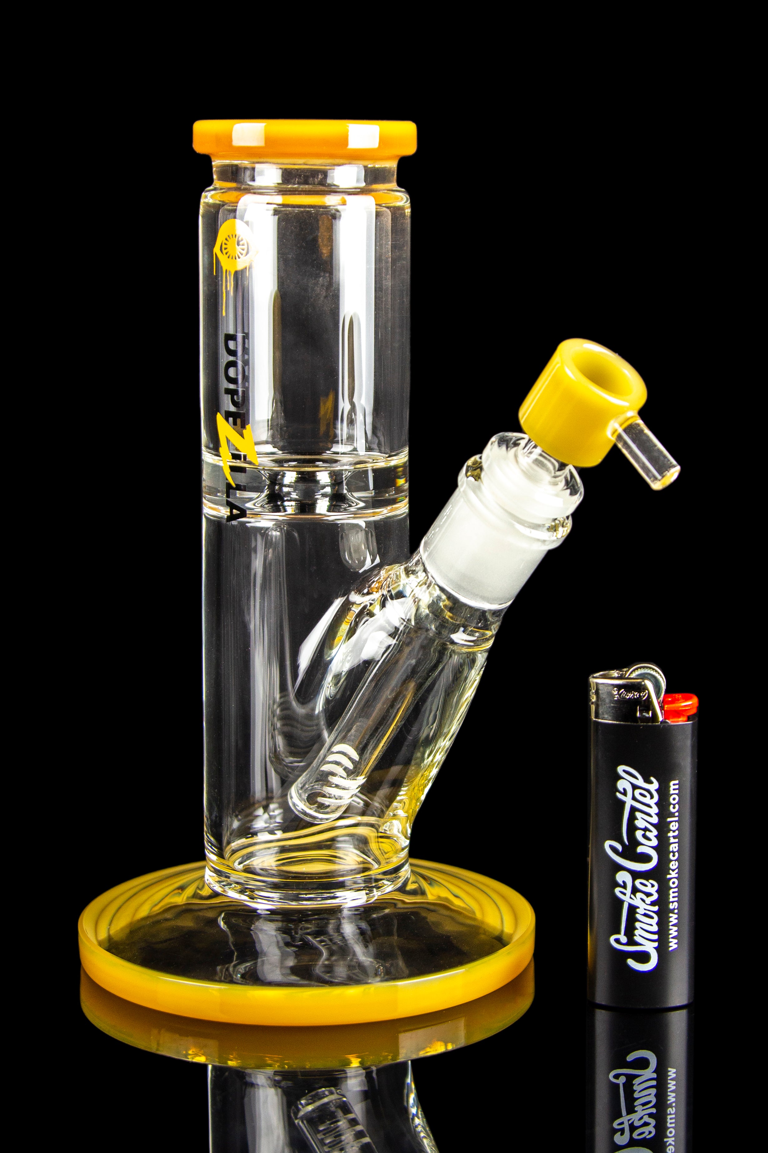 A clear glass bong with yellow accents, a glass bowl, and a lighter, displayed on a reflective surface.