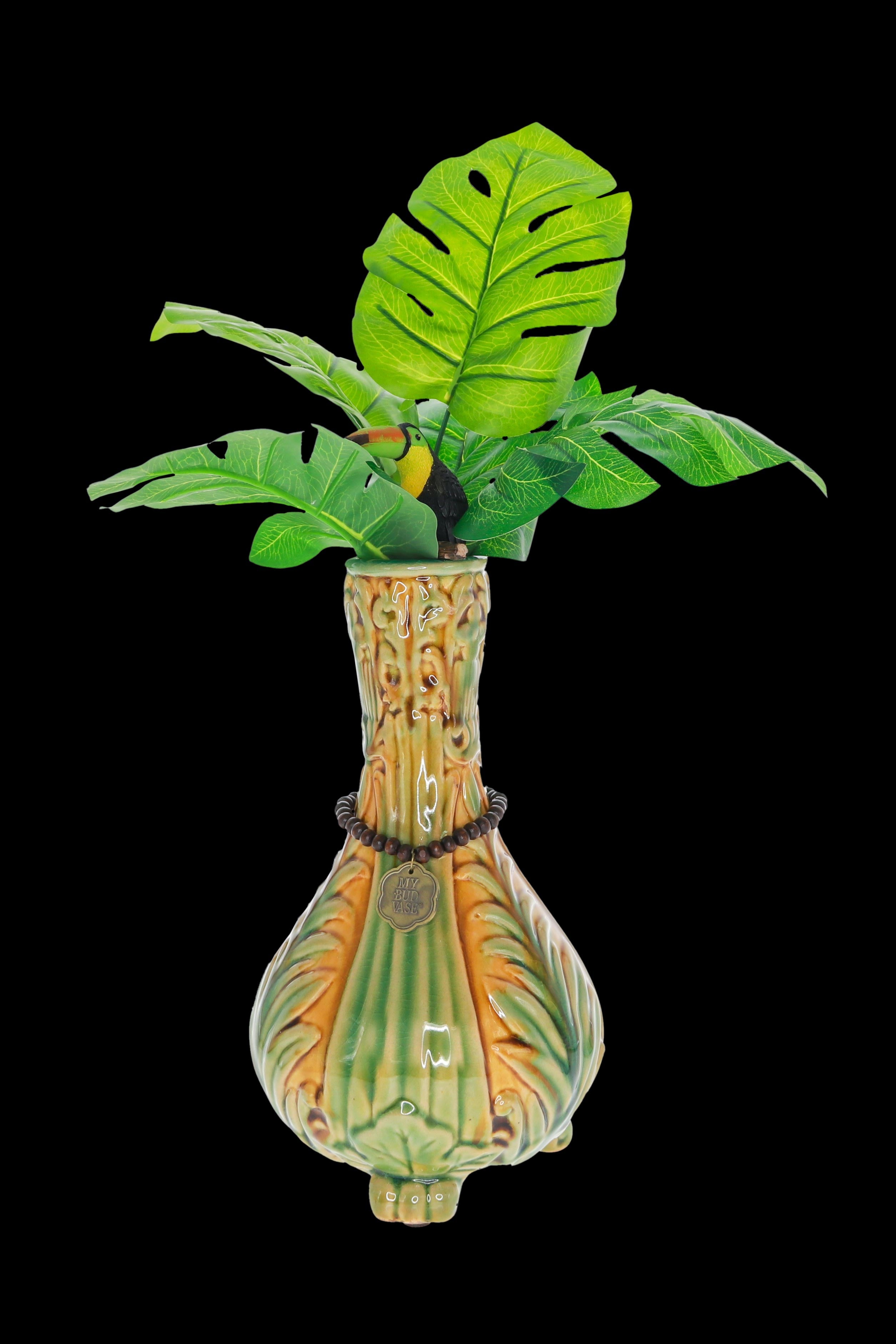 A vibrant, tropical-themed glass water pipe shaped like a gourd, adorned with sculpted leaves and a toucan perched amidst lush, artificial foliage.