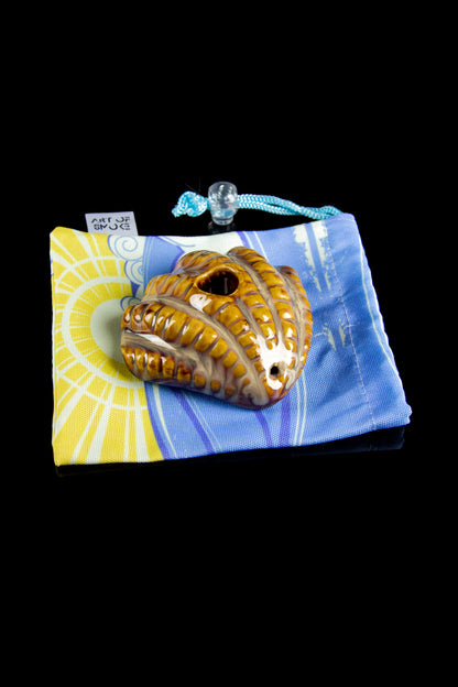 A close-up shot of the Art of Smoke Clamshell Pipe resting on a patterned blue and yellow cloth.