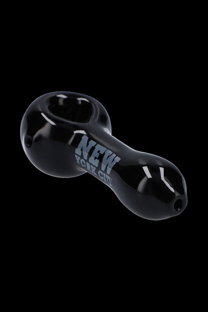 Angled close-up of the black Rock Legends Glass Spoon Pipe - Jimi NYC against a solid black background showing glossy reflections and "NEW YORK CITY" text.