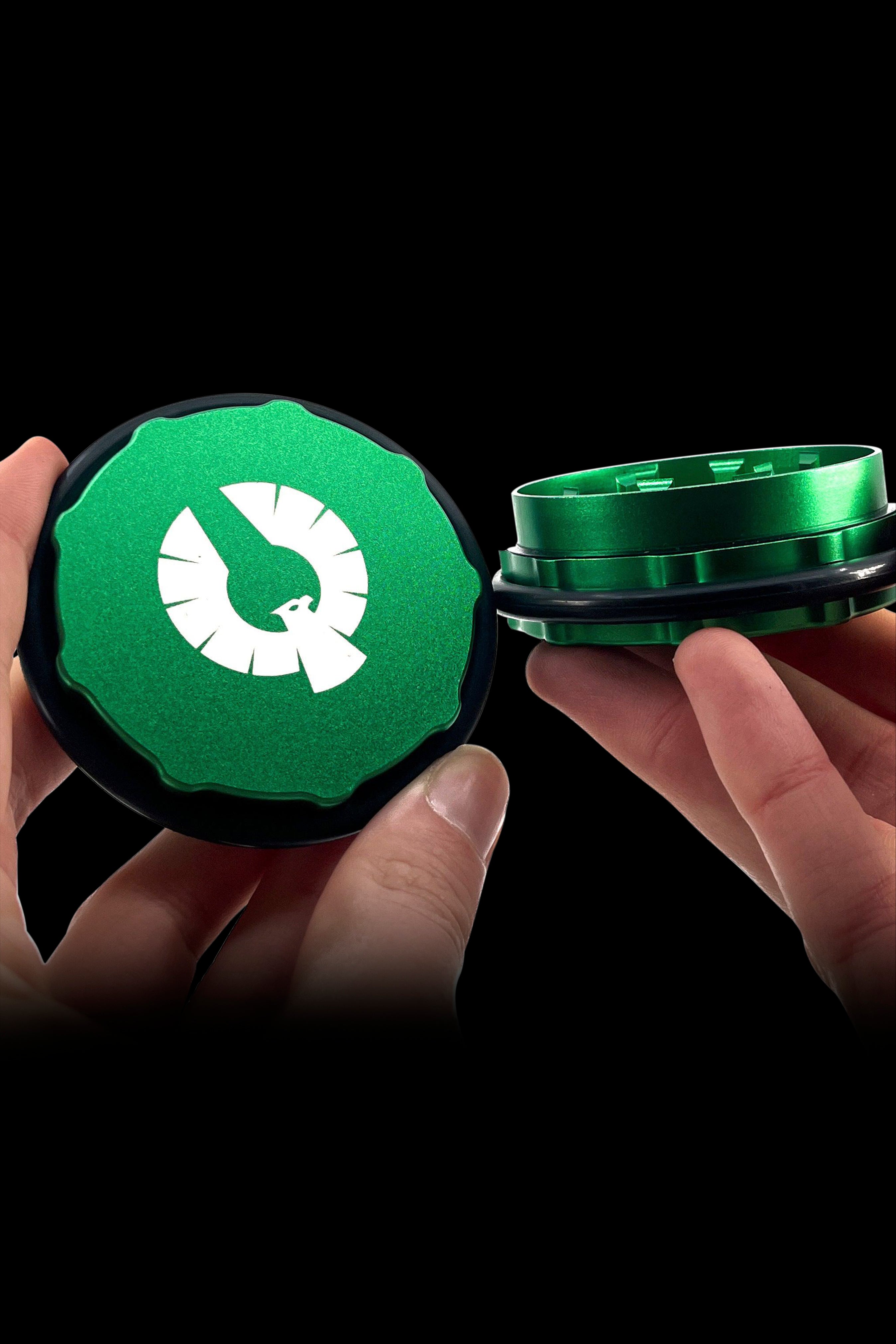 Hand holding open a green grinder for cannabis, revealing the inner grinding chamber.