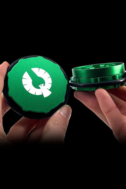 Hand holding open a green grinder for cannabis, revealing the inner grinding chamber.