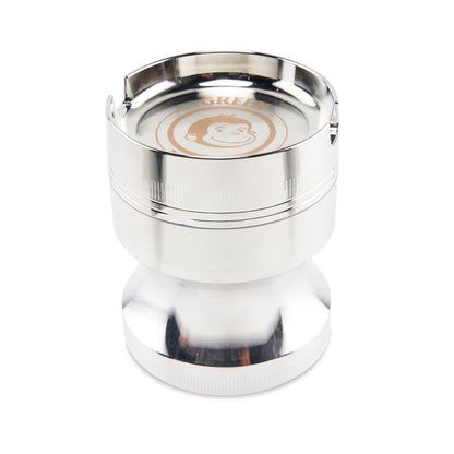 Close-up top-down view of the metallic Green Monkey Chacma Grinder with Ashtray showing its shiny rim, slot notches, and stamped monkey logo.