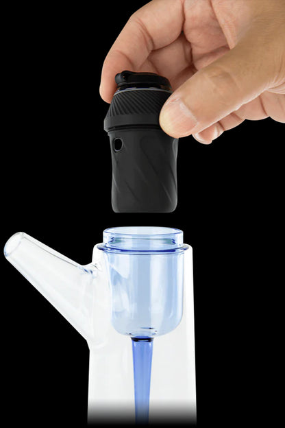 A hand holding a black cannabis vaporizer over a blue glass bubbler water pipe.