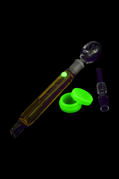 Glowing glass dab rig with oil and accessories on a black background.