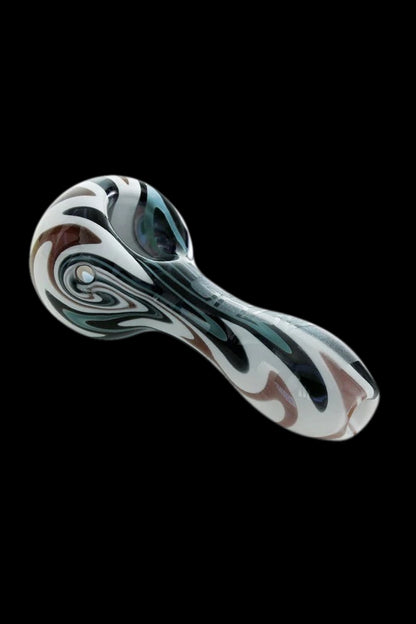 Glass pipe with swirling black, white, and brown patterns against a black background.