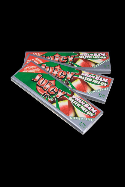 Close-up of Juicy Jay's Superfine 1-1/4" flavored rolling papers stacked on a dark surface, showing colorful patterned designs.