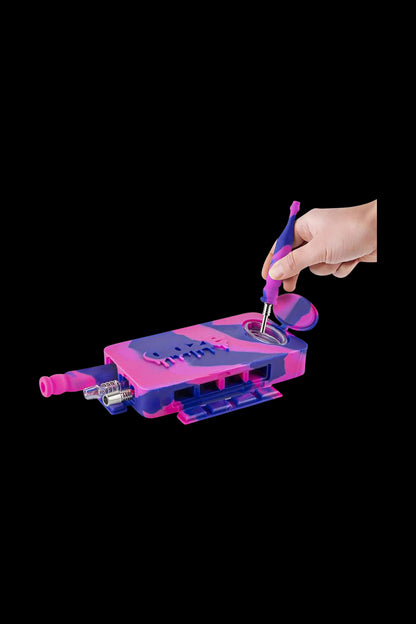 A hand holds the Ooze Slugger Dabbin Dugout, featuring a purple and blue design, angled towards the viewer on a dark background.