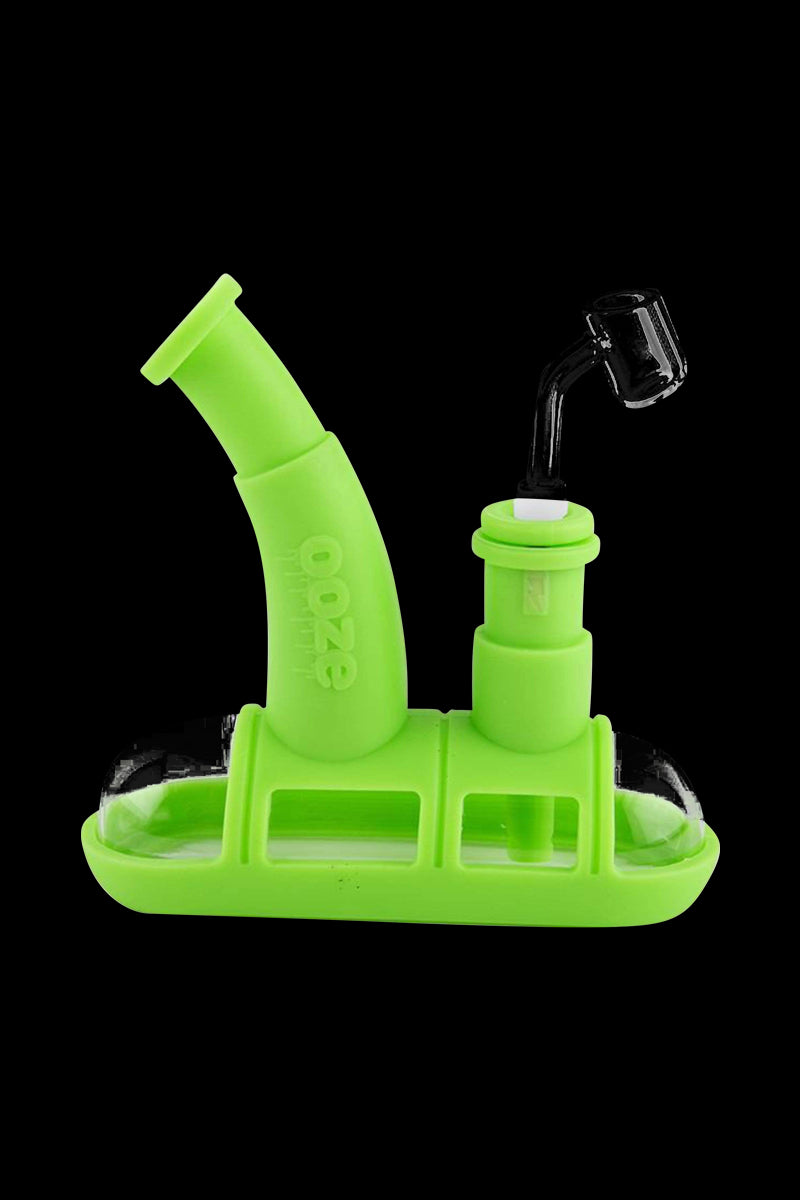 A studio shot of the Ooze Steamboat Silicone Bubbler Boat Bong, showcasing its bright green, boat-shaped design against a dark backdrop.