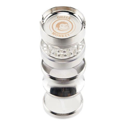 Top-down view of a disassembled stack of the Green Monkey Chacma Grinder with Ashtray showing its metallic chambers, teeth, mesh screen, and branded lid.